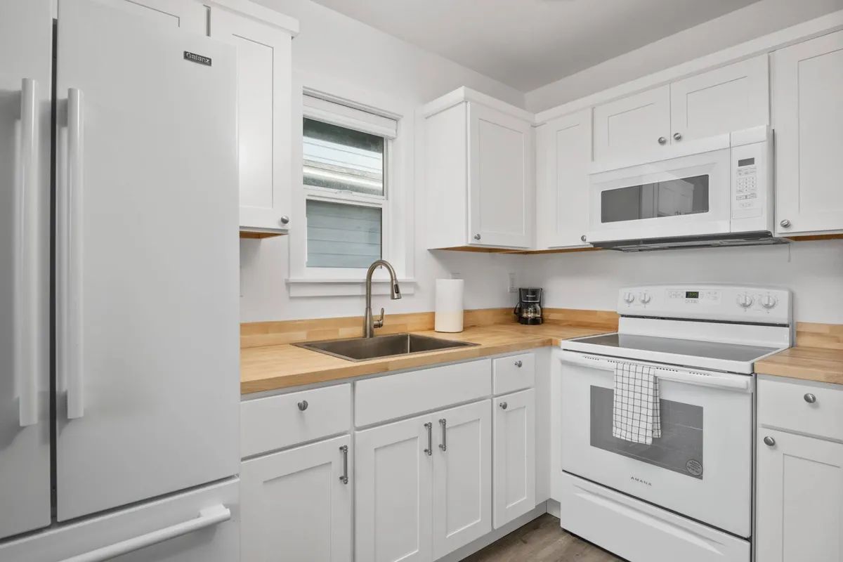 A modern, fully-equipped kitchen with white cabinetry, stainless steel appliances, a wooden countertop, and a sleek sink. The space is functional yet stylish, ready for preparing home-cooked or seaside-inspired meals. The lack of a dishwasher is not visually apparent, keeping the scene uncluttered and focused on the kitchen’s inviting appeal.