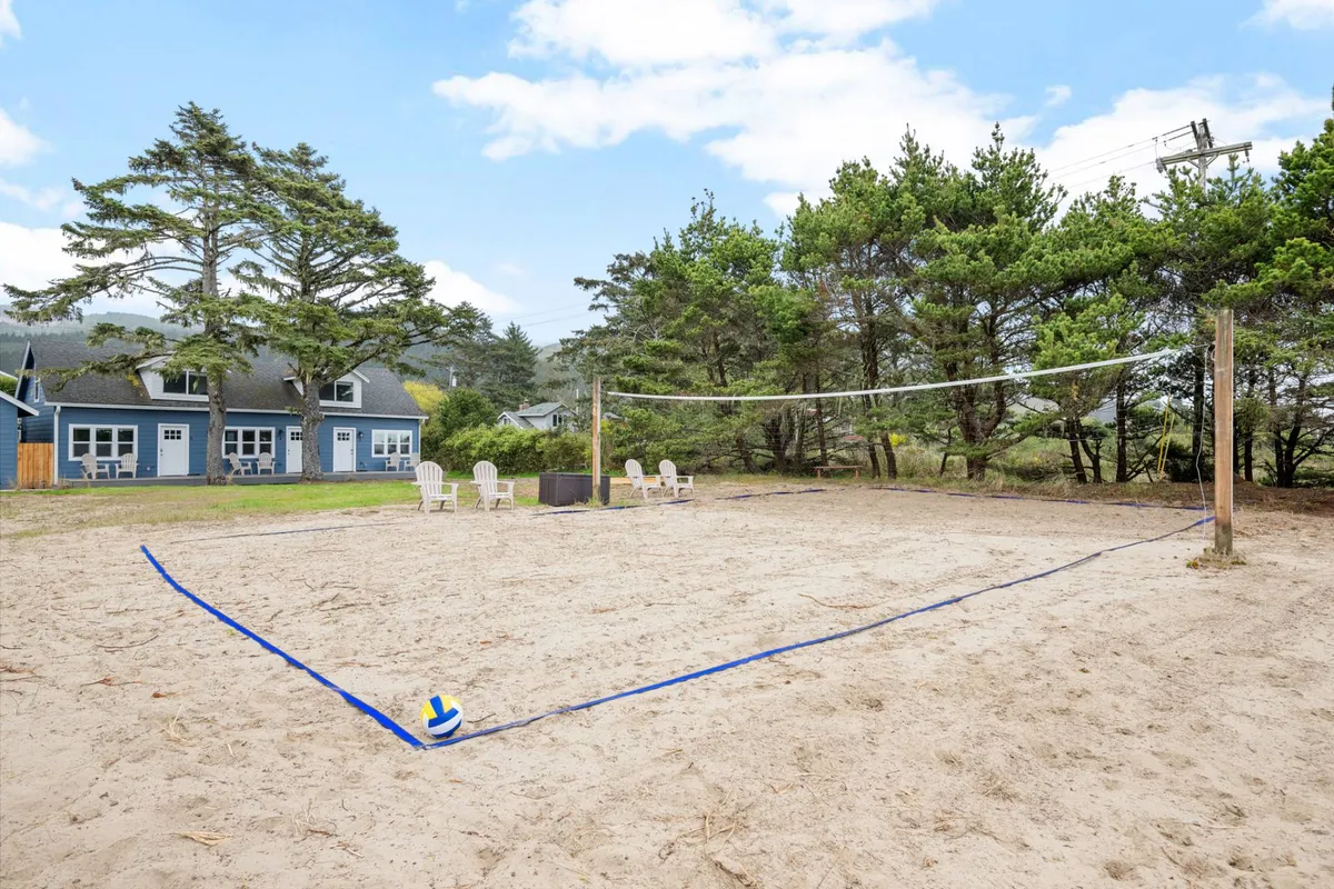 A lively exterior view of the inn’s sand volleyball court, surrounded by lush trees and a bright blue sky. The seating area nearby invites guests to relax and socialize after a game, capturing the playful energy and communal spirit of the outdoor amenities.