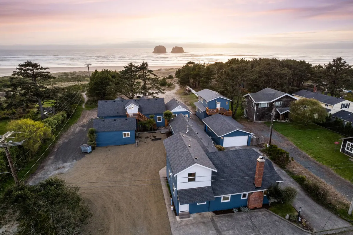 A peaceful beachfront scene with sandy shores, natural rock formations, and distant views of houses and trees. The image evokes the tranquility of direct beach access, inviting guests for scenic walks or playful adventures by the ocean.