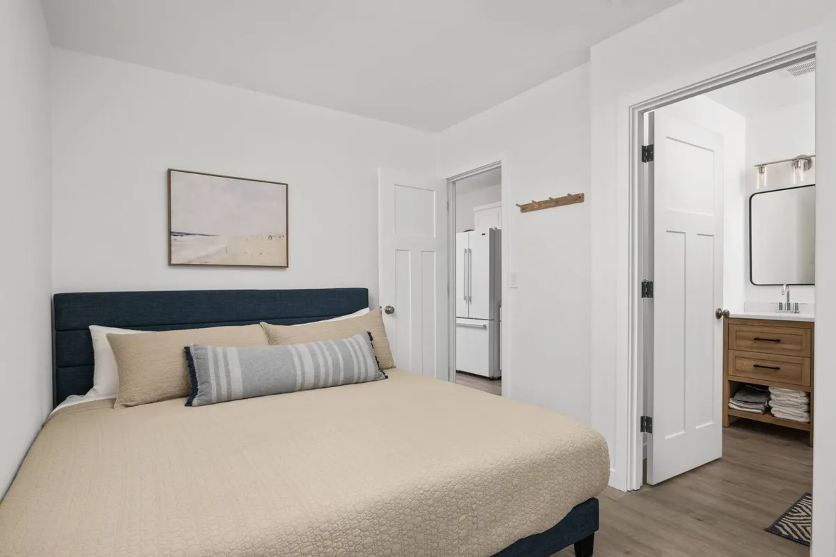 A serene interior photo emphasizing a bed with beige bedding, complemented by tasteful artwork and doorways leading to other rooms. The room is bathed in gentle natural light, evoking a relaxing and cozy atmosphere ideal for restful sleep. This reflects the tranquil environment described.