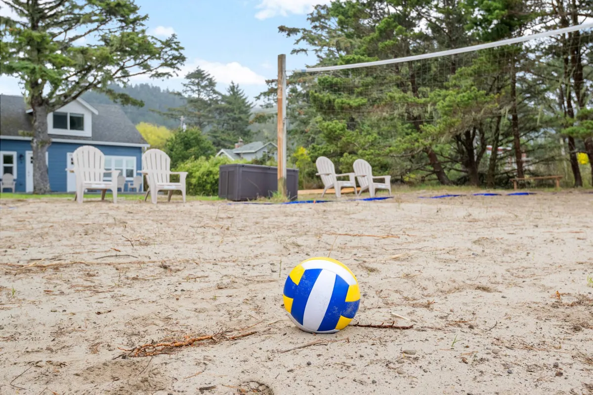 A playful and active space showing a volleyball net, a ball mid-game, beach chairs, and surrounding trees, all bathed in warm natural light. The seating invites onlookers and participants alike to join in or enjoy the atmosphere.