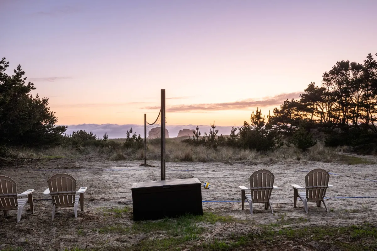 A vibrant beachfront scene with Adirondack chairs facing a volleyball net, the ocean stretching beyond and a dramatic sunset sky overhead. The area is designed for both relaxation and active play, perfectly blending social opportunities with scenic views.